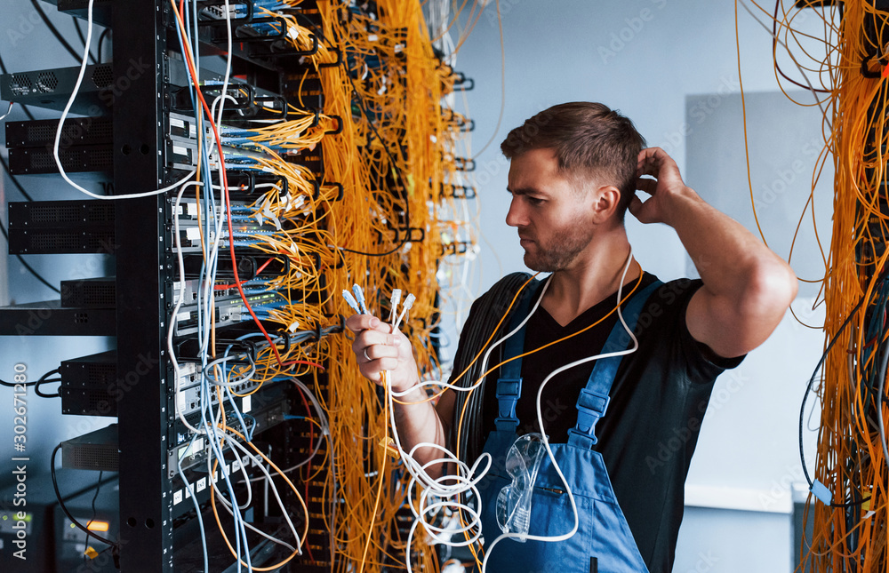 Wall mural young man in uniform feels confused and looking for a solution with internet equipment and wires in 