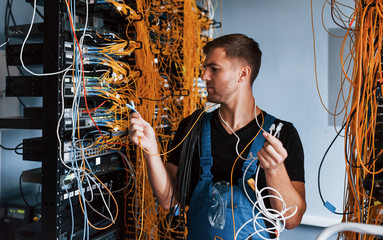 Young man in uniform feels confused and looking for a solution with internet equipment and wires in...