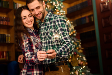 Sparklers and a kiss for Christmas! Young beautiful kisser and burning sparklers. Loving couple  in Christmas decorated room.
