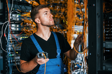 Young man in uniform have a job with internet equipment and wires in server room