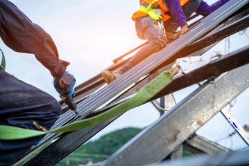 Roofer worker in special protective work wear and gloves,Using pneumatic gun and installing Metal...