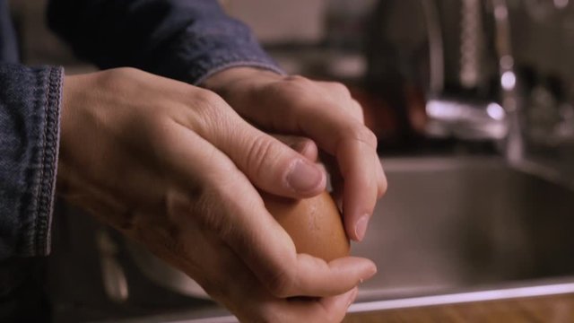 Peeling an egg in the kitchen next to a sink.