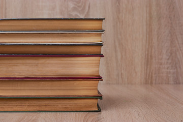 A stack of old books of different colors on a beige background. Yellow faded pages of the book,...