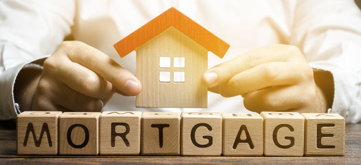 Wooden blocks with the word Mortgage and house in the hands of a businessman. The concept of buying...