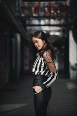 street portrait, strong woman in black, confident woman, lady in city, portrait of Asian female, half body, standing looking at the ground and hand in pocket wearing stripe top
