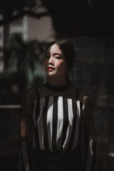 street portrait, strong woman in black, confident woman, lady in city, portrait of Asian female, half body turning half face to the sunlight wearing stripe top