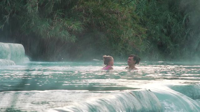 Young Mother and Daughter Swimming and Relaxing in Hot Springs of Saturnia, Grosseto, Tuscany, Italy. Natural Spa with Waterfalls and Thermal Waters. Relax and Spa Concept