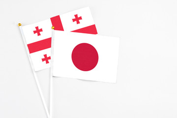 Japan and Georgia stick flags on white background. High quality fabric, miniature national flag. Peaceful global concept.White floor for copy space.