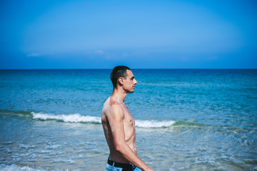 Fototapeta na wymiar young muscular man resting and posing on the beach. A young man walks by the sea