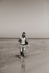 young muscular man resting and posing on the beach. A young man walks by the sea