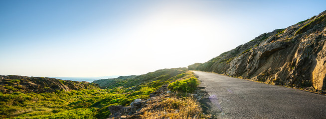 Empty long mountain road to the horizon on a sunny summer day at bright sunset - obrazy, fototapety, plakaty
