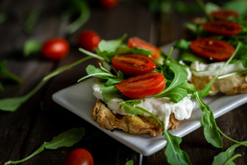 Mozzarella, arugula and cherry tomatoes Bruschetta on a rustic table