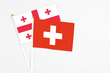 Obraz premium Switzerland and Georgia stick flags on white background. High quality fabric, miniature national flag. Peaceful global concept.White floor for copy space.