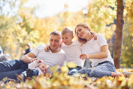 Cheerful young family lying down on the ground and have a rest in an autumn park together