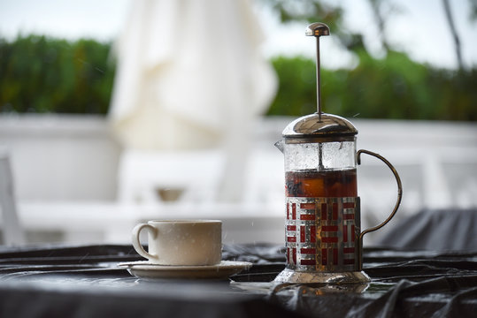 Glass teapot with tea and cup on a table in a street cafe in the rain. Raindrops falling on the table.