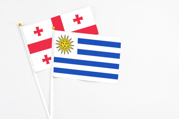 Uruguay and Georgia stick flags on white background. High quality fabric, miniature national flag. Peaceful global concept.White floor for copy space.