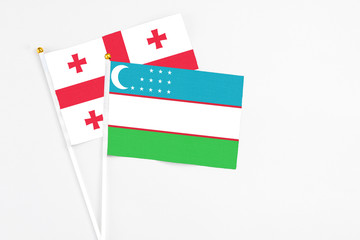 Uzbekistan and Georgia stick flags on white background. High quality fabric, miniature national flag. Peaceful global concept.White floor for copy space.