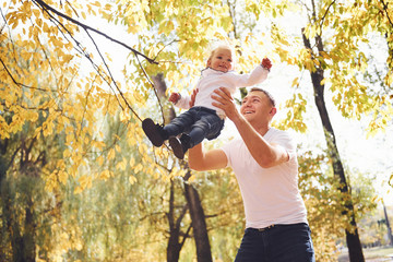 Dad holds his daughter in hands and have fun in the autumn park