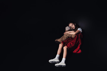 lonely child lying on floor and embracing teddy bear on black background