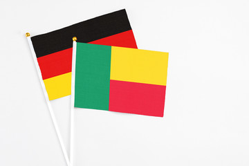 Benin and Germany stick flags on white background. High quality fabric, miniature national flag. Peaceful global concept.White floor for copy space.