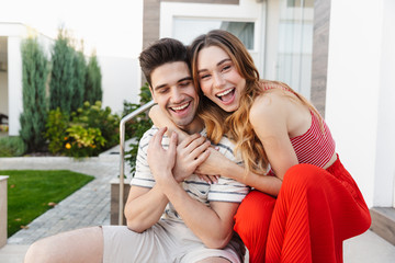 Image of pleased beautiful couple laughing and hugging while sitting