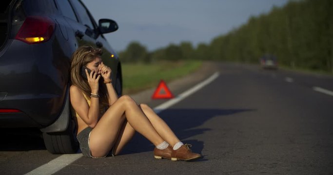 a young woman call on the phone, a broken car on the road in the frame on the emergency