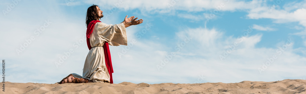 Wall mural panoramic shot of jesus praying on knees in desert against sky