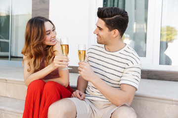 Image of young beautiful couple smiling and drinking wine while sitting