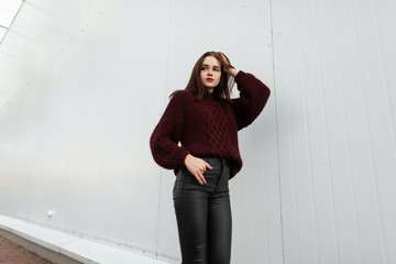 European pretty young fashionable woman in a stylish burgundy sweater in trendy black leather pants...