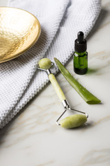 Massage Steinroller, Aloe Vera Blatt und Naturkosmetik Beauty Öl Serum Flasche grün an Handtuch, Gold Metall Schale und Marmor Hintergrund 