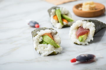 Lachs, Tunfisch und Surimi Avocado Temaki Sushi, eingelegter Ingwer mit Soja Soße Fische und Sushimatte auf Marmor Hintergrund