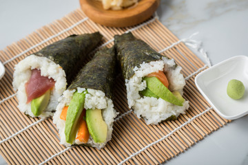 Lachs Fisch, Tunfisch und Surimi Avocado Temaki Sushi, eingelegter Ingwer mit Soja Soße und Sushimatte auf Marmor Hintergrund