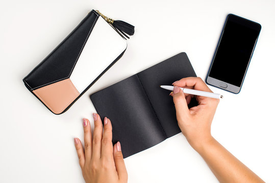 Female hand writting on a black notebook, top view. Fashion style, woman workplace background for blogging. Flat lay. Fashion blooger workplace
