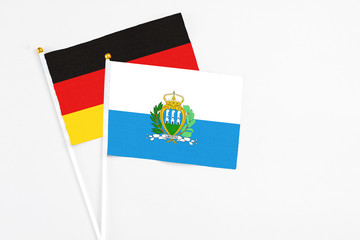 San Marino and Germany stick flags on white background. High quality fabric, miniature national flag. Peaceful global concept.White floor for copy space.