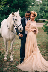 Newlyweds are standing near a white horse in nature