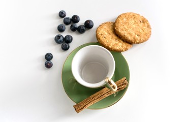 Green vintage tea cup , blueberries, cinnamon stick and cookies against white background. Breakfast, food and infusion concept.