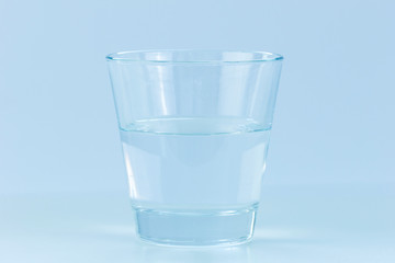 Close-up of a transparent drinking glass half full or empty of water. Concept photo of positive or negative attitude. Blue hue.