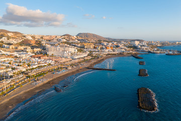 Fototapeta na wymiar Drone aerial shot of Costa Adeje area, South Tenerife, Spain. Captured at golden hour, warm and vivid sunset colors. Luxury hotels, villas and restaurants behind the beach.