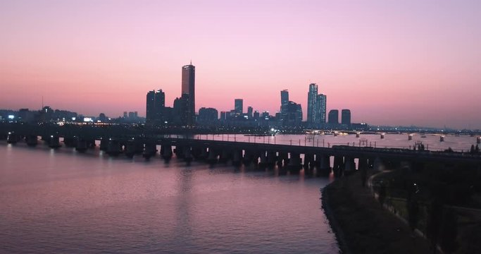 Still shot - Drone Aerial footage of a train crossing in front of buildings in Seoul, South Korea - Sunset