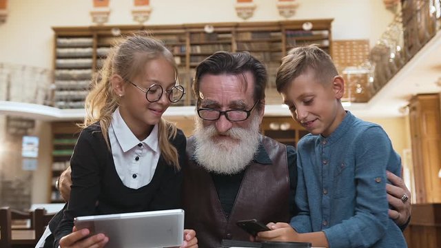 Smiling happy grandfather with grandchildren cheerfully spending their time together in the library