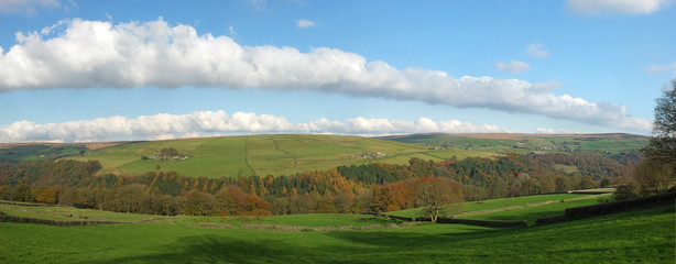 wide panoramic view of west yorkshire countryside with the forest of hardcastle crags in the bottom of a wide valley surrounded by meadows with grazing sheep in bright autumn sunshine
