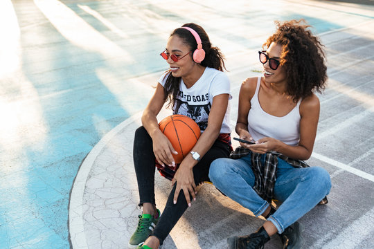 Image of african american girls sitting on playdround with basketball