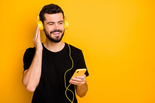 Portrait of positive cheerful guy have spring weekends listen music use modern headset from his smartphone wear good looking isolated over yellow color background