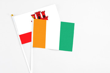 Cote D'Ivoire and Gibraltar stick flags on white background. High quality fabric, miniature national flag. Peaceful global concept.White floor for copy space.