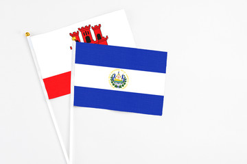 El Salvador and Gibraltar stick flags on white background. High quality fabric, miniature national flag. Peaceful global concept.White floor for copy space.