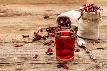 Hot hibiscus tea. Dry petals, linen sacks. Healthy food and self-care concept. Old wooden boards...