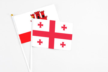Georgia and Gibraltar stick flags on white background. High quality fabric, miniature national flag. Peaceful global concept.White floor for copy space.
