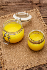 Pure or desi ghee (ghi), clarified melted butter. Healthy fats bulletproof diet concept or paleo style plan. Glass jar, silver spoon on vintage sackcloth. Wooden boards background