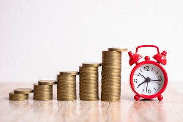 A red alarm clock and a pile of coins resting on the table. Ideas to save money, ideas for business growth, use the right time to invest, the idea of using time to be worth the money. Investment risk.