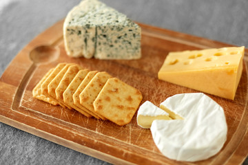 food and eating concept - different kinds of cheese and salty crackers on wooden cutting board